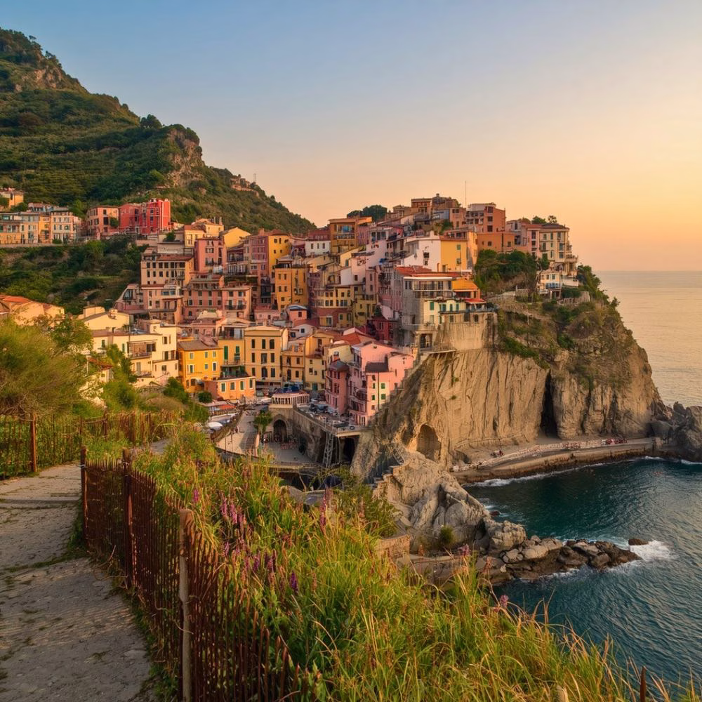 Cinque Terre hiking trail above the sea, leading to a cliffside village at sunset