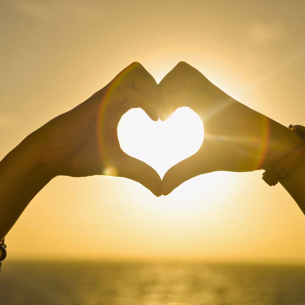 Hands forming a heart against a sunset over the sea, the spirit of giving behind La Spezia events